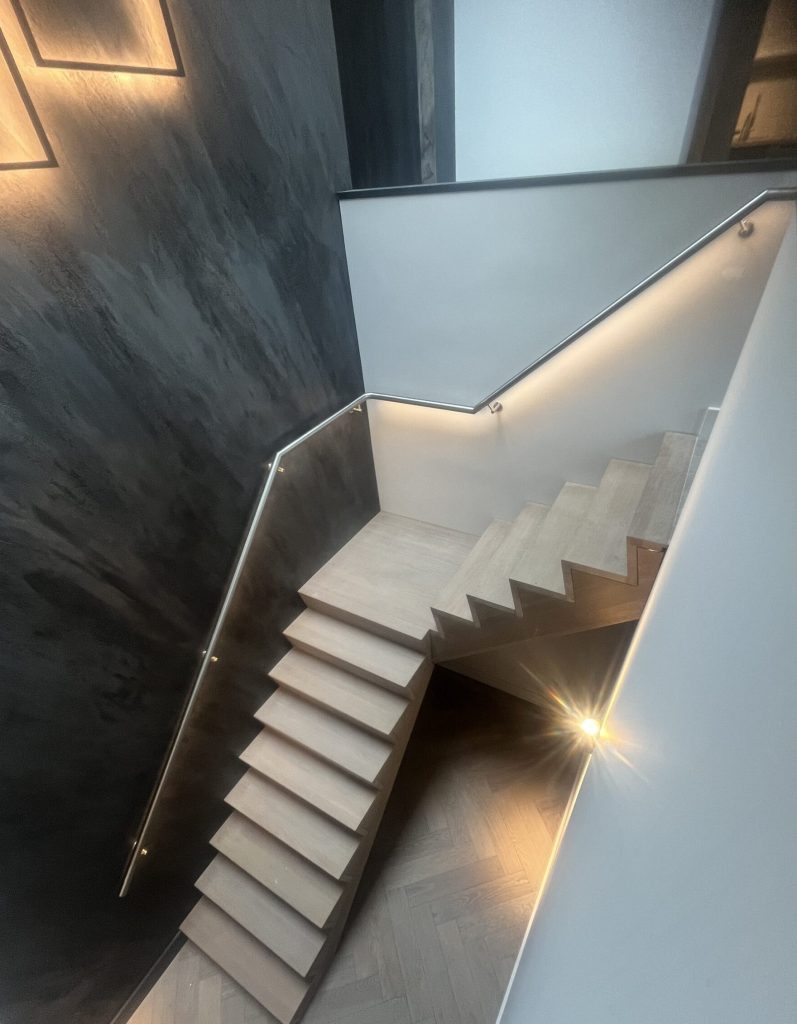 RVS trapleuning met LED‑verlichting langs houten trap in moderne woning