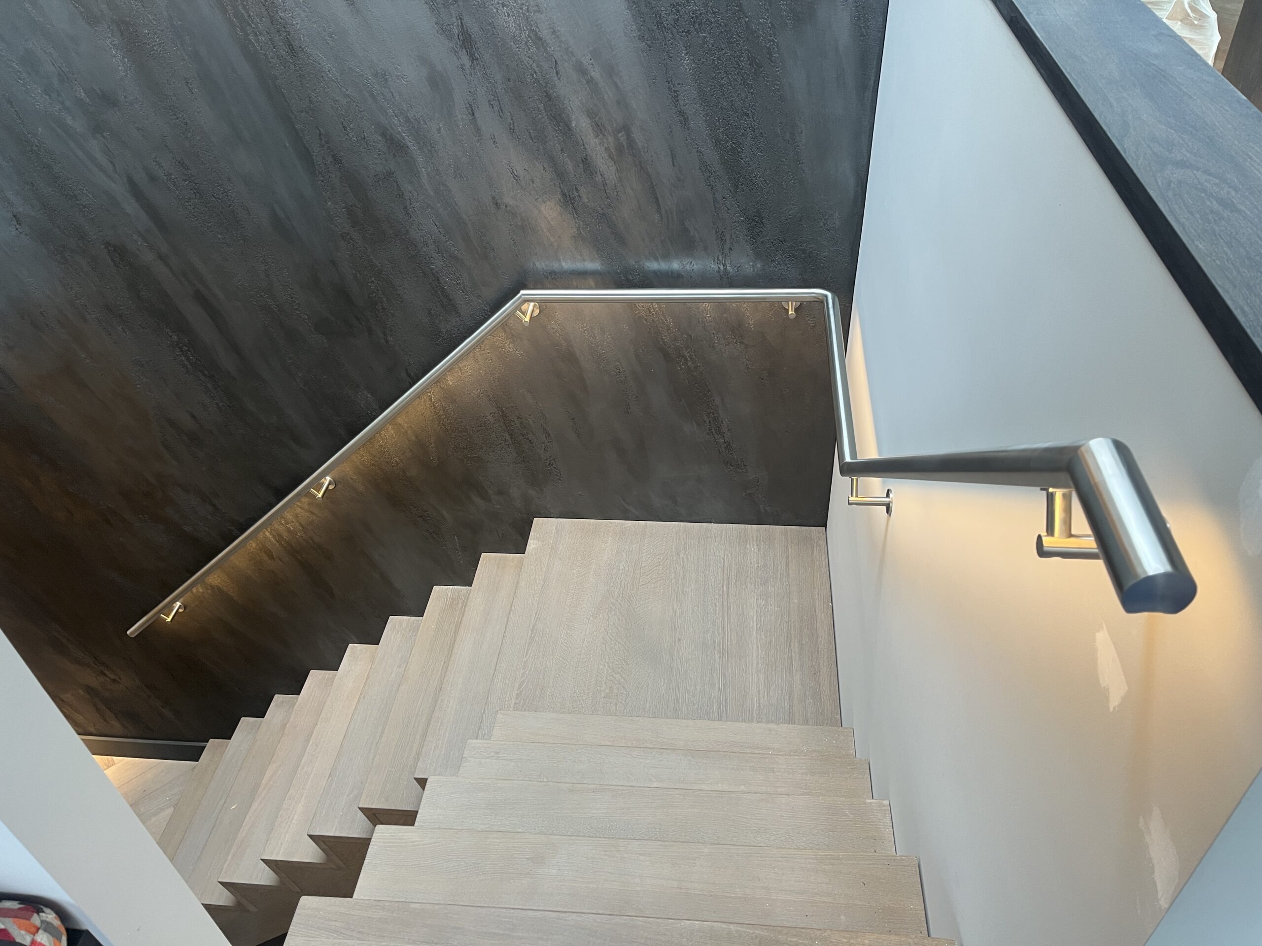 Modern trappenhuis met RVS trapleuning en warm‑witte, dimbare LED‑verlichting
